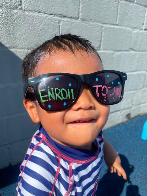 A grinning child wearing oversized novelty sunglasses that read Enroll Today.