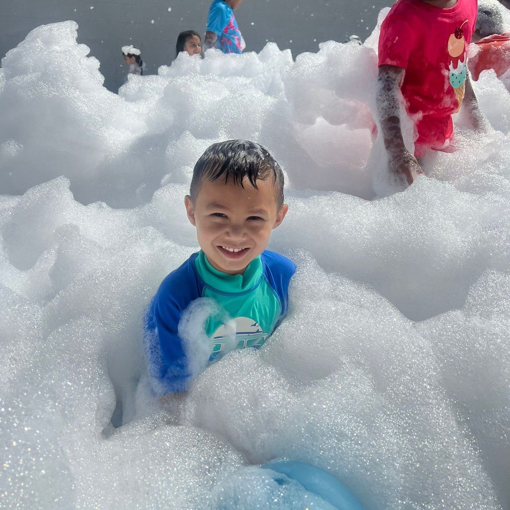 Children playing in a mound of soap foam outdoors.