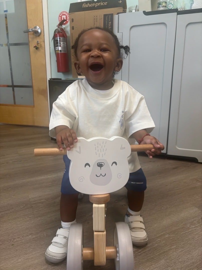 A laughing infant on a ride-on toy in the ESPIN infant room.