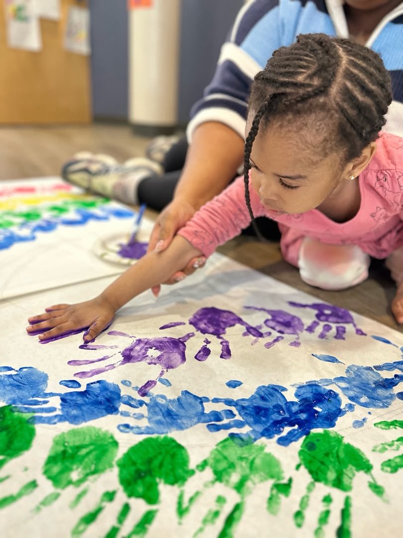 A child pressing painted handprints onto a large sheet of paper.